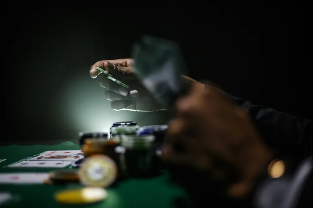 Eine Person hält einen Pokerchip, während ein Lichtstrahl auf ihn scheint und ihn hervorhebt. 
